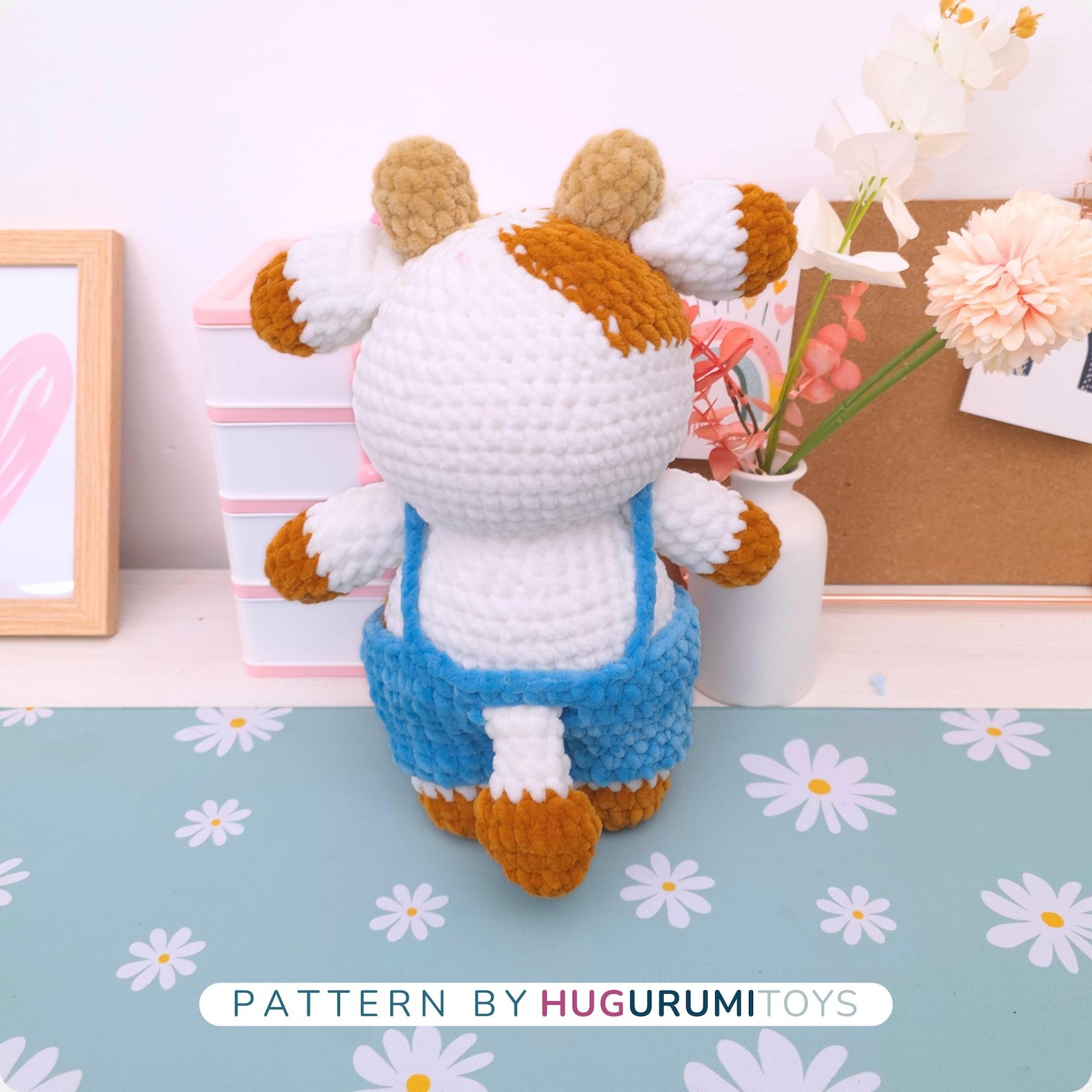 Amigurumi crochet cow wearing blue overalls sitting on a white background – view 3